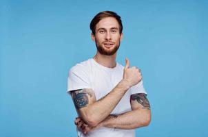 alegre hombre con tatuajes en su brazos en un blanco camiseta en un azul antecedentes foto