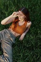 The view from above is a woman lying on the green grass in the park and relaxing in nature smiling and enjoying life. The concept of a healthy lifestyle photo