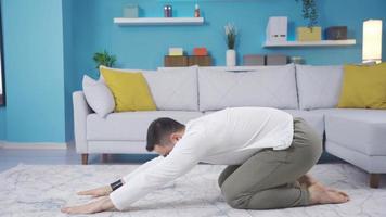 Fitness instructor showing how to do balasana at home looking at camera. Young fitness instructor doing warm-up and stretching exercises at home, balasana, teaching his students. video