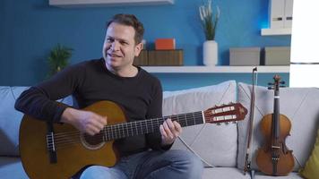 contento músico hombre jugando su guitarra a hogar sonriente felizmente, disfrutando su violín. video