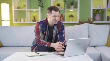 glücklich und lächelnd Mann Arbeiten von Zuhause mit Laptop. Mann Arbeiten von Zuhause auf Laptop ist im ein gut Stimmung und lächelnd. video