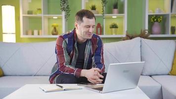 feliz e sorridente homem trabalhando a partir de casa usando computador portátil. homem trabalhando a partir de casa em computador portátil é dentro uma Boa humor e sorridente. video