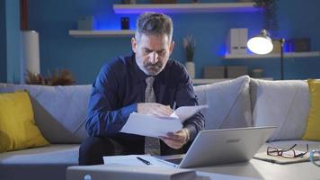 Focused businessman carefully reading document, working papers and laptop seriously and professionally. video