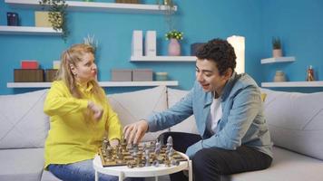 heiter und glücklich reifen Frau und ihr Sohn spielen Schach zusammen beim heim. heiter und komisch jung Mann schlägt seine Mutter beim ein Spiel von Schach und macht Spaß von ihr.