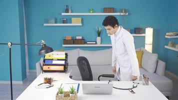 Dreamy boy at home sitting at desk with white doctor coat and stethoscope. Funny boy in doctor uniform and stethoscope sitting at the working table of his doctor parents. video