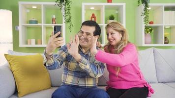 man och kvinna framställning mobil video ring upp i virtuell app med smartphone i hand. farfar och mormor är video chattar med deras barnbarn och barn på Hem, de är Lycklig.