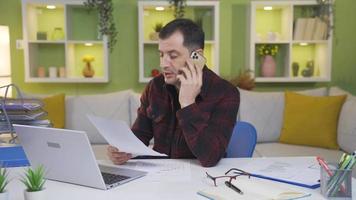 Man working from home talking about work on the phone while checking out. While the man is running his business from his home, he is also making business calls on the phone. video