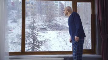 el antiguo hombre, profundo en pensamiento, por el ventana en el invierno, avisos su joven nieto. mientras el abuelo es mirando fuera el ventana con nostalgia y pensamiento, su nieto viene y ellos charlar. video