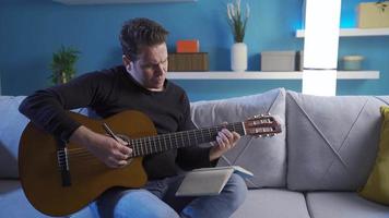 Songwriter man creating a new composition plays the guitar alone at home, writes the lyrics in a notebook. video