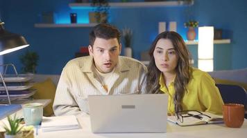 a casado casal concentrando em a computador portátil tela estão chocado de o que elas ver. video