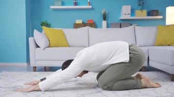 Young man doing warm-up and stretching exercises at home, doing balasana. Young man exercising at home doing balasana, relaxing and stretching his body. video