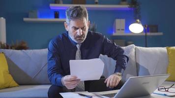 maduro empresario mirando cuidadosamente a trabajo documentos y ordenador portátil seriamente y profesionalmente recibe malo noticias. video