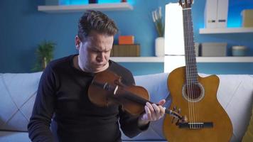 triste homem jogando acústico guitarra às lar. infeliz homem sentado em sofá. solitário homem jogando guitarra. video