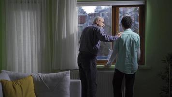 Grandpa and grandchild get along well. Family love. The old grandfather looks out of the window with his grandson, they chat, the grandfather gives advice to the grandchild. video