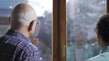 Elderly grandfather and grandson happily chatting in front of the window. The old grandfather and his grandson are having a pleasant conversation in front of the window. video