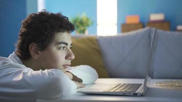 gelukkig en vrolijk jongen op zoek Bij laptop met focus. puber mannetje aan het kijken films Aan laptop Bij huis, aan het kijken documentaires, op zoek Bij de foto van zijn vriendin. video