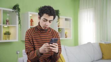 frustrado adolescente chico, aburrido chico. un chico mirando a su teléfono inteligente a hogar recibe malo y triste Noticias y es deprimido. video