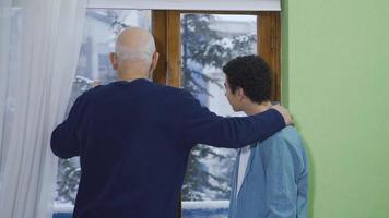 The old grandfather brings his grandson to the window and tells his memories of his past in the view of falling snow. video