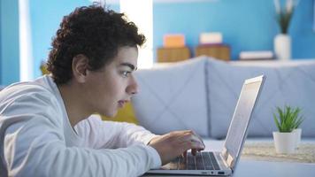 adolescente masculino procurando a Internet e sites. feliz e alegre adolescente masculino usando social meios de comunicação, virtual mundo e Internet a partir de computador portátil às lar. video