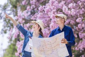 Asian couple tourist holding city map while walking in the park at cherry blossom tree during spring sakura flower festival concept photo