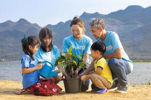 equipo de voluntario trabajador grupo enseñando niños a plantando árbol en Caritativo social trabajo en bosque reconstrucción ong trabajo para luchando clima cambio y global calentamiento en el línea costera habitat foto