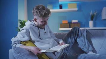 The young man reading quietly and calmly at home is happy and pleasant. Charming handsome young man reading a book at home alone in peace and happiness. video