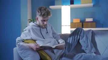 contento y hermoso joven hombre leyendo un libro pacíficamente a hogar solo. joven hombre leyendo libro, teniendo divertido, leyendo novedoso, libro magia. video