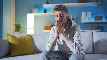 Depressed young man is not happy, disappointed, helpless and sad. The young man, alone at home, is feeling sad, looking at the camera, suffering from unhappiness. video