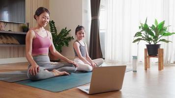 asiatisk mor och dotter omfamning sinne-kropp förbindelse med virtuell yoga kurs på bärbar dator video ring upp