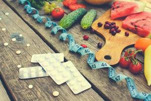 Fruits, vegetables, measure tape, pills on wooden background. Concept of different ways to lose weight. Toned image. photo