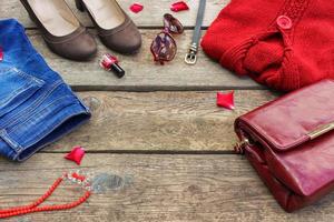 Women's autumn clothing and accessories red sweater, jeans, handbag, beads, sunglasses, nail polish, shoes, belt on wooden background. Top view. photo