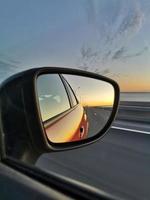 Reflection of road and sunset in the side mirror of the orange car. Concept of road trip and traveling by car. photo