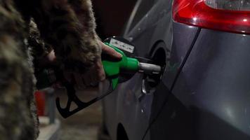 Woman inserts a fuel gun in a gas tank to refuel a car. Concept of increasing gasoline prices, fuel crisis video