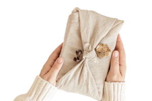 Beige cloth wrapped a gift held by a woman's hands isolated on a transparent background png