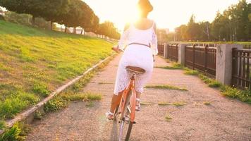 giovane bellissimo donna seduta su sua bicicletta con fiori a tramonto video