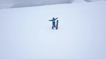 Flight over the man with a snowboard which stands on top of a snow-capped mountain. Uncomfortable unfriendly winter video