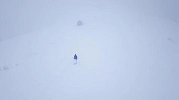 Flug Über das einsam Tourist Mädchen Gehen entlang das oben von ein Berg bedeckt mit Schnee. unbequem unfreundlich Winter Wetter. video