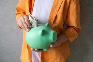 A piggy bank in the hands of a boy in a shirt. Put a banknote in a piggy bank photo