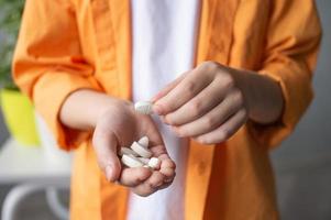 A child in an orange shirt holds a lot of pills in his palm photo