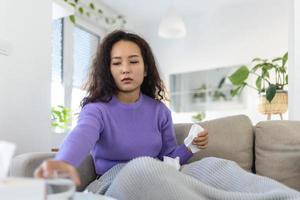 Sick desperate woman has flu. Rhinitis, cold, sickness, allergy concept. Asian sick woman has runnning nose, rubs nose with handkerchief. Sneezing female. Brunette sneezing in a tissue photo