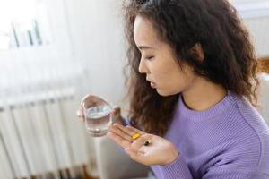 Asian ill sick woman taking painkiller medicine to relieve stomachache pain sit on bed in the morning. Sick woman lying in bed with high fever. Cold flu and migraine. photo