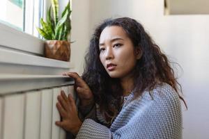 Asian Woman freezing at home, sitting by the cold radiator. Woman with home heating problem feeling cold photo