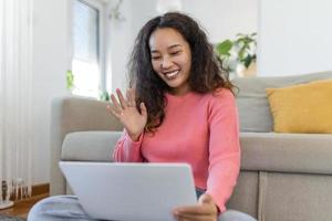 Asian woman waving at laptop and talking to her friends via video call, girl student talking by video conference call, female teacher trainer tutoring by webcam, online training, e-coaching concept photo