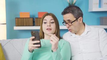 padre y hija mirando a el teléfono juntos. padre y hija chateando mientras utilizando el teléfono. ellos son contento. video