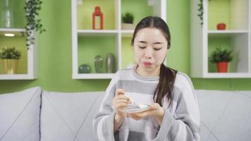 Happy and cute asian young woman eating yogurt. Young Asian woman eating yogurt at home meets her protein and calcium needs. video