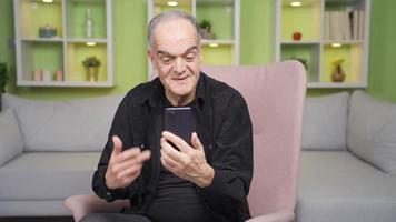 Old man using phone confused and talking to himself. The old man using the phone is surprised by what is going on on the phone and talks to himself. video