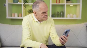 The old man gets angry at what he sees on his phone at home. While the old man is using his smartphone at home, he gets angry and depressed at the news he receives or the videos he sees.