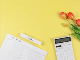 flat layout of Habit tracker book,  white calculator, wooden calendar May and tulips on yellow background. photo