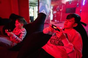 Two boys gamers play gamepad video game console in red gaming room. photo