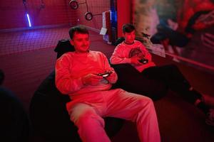 Father and son play gamepad video game console in red gaming room. Dad and kid gamers. photo